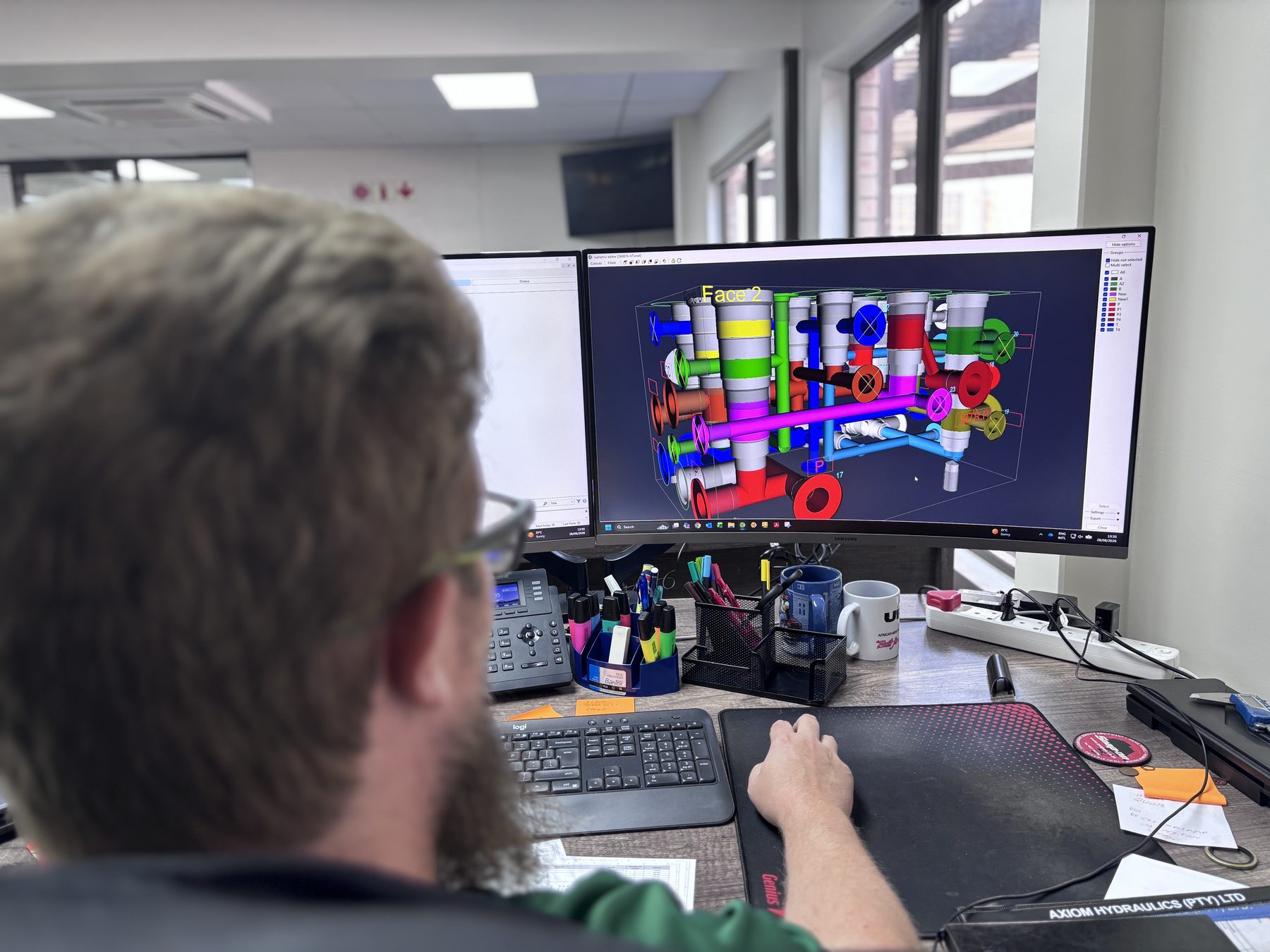 Axiom Hydraulics designer modelling a hydraulic manifold circuit in 3D at a dual-screen Design House workstation