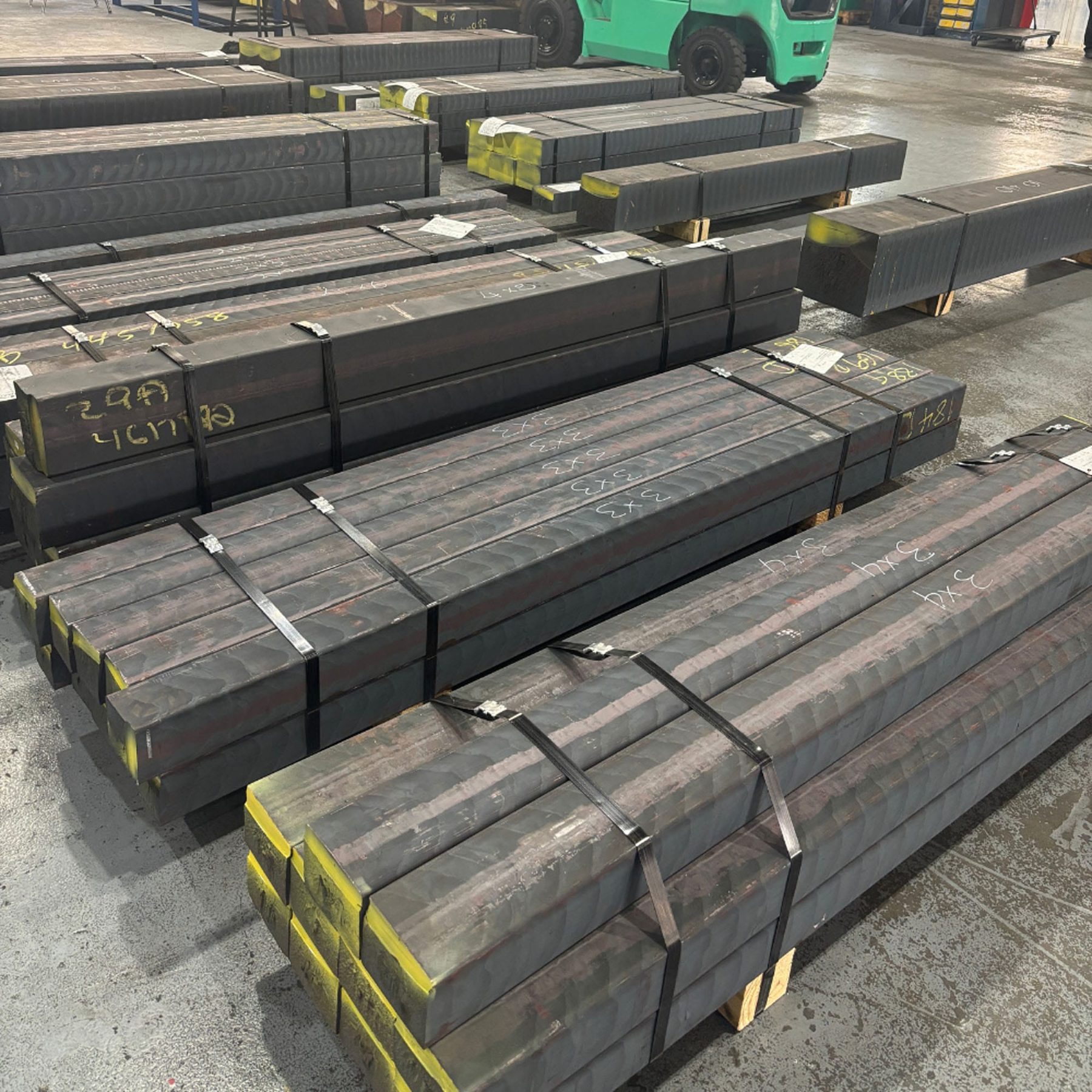 Bundled square Dura-Bar bar stock stacked in a warehouse with a forklift in the background